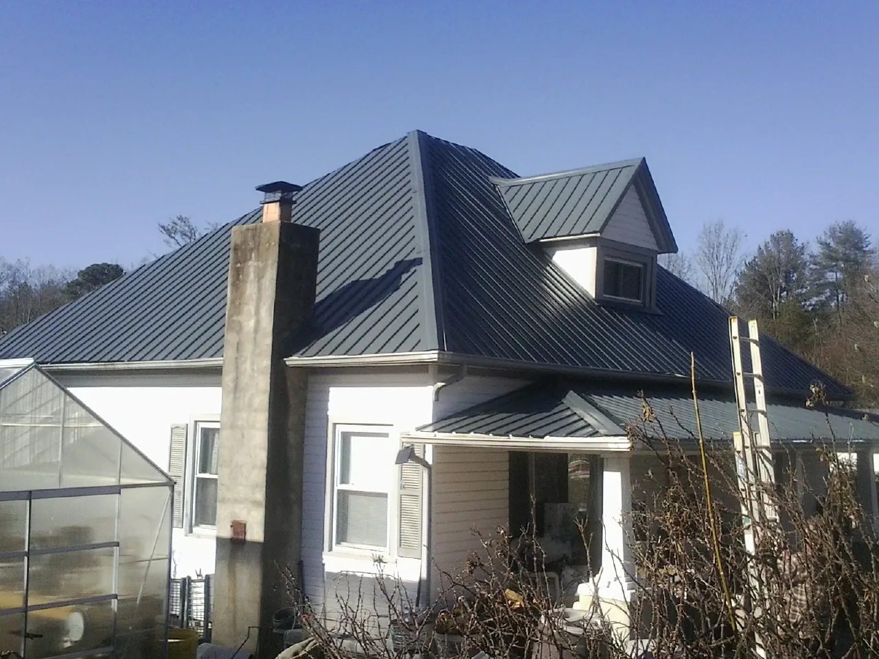 Dark blue standing seam metal roof on a white farmhouse with dormer — Slate & Tile Roof Repair by Roofing Brothers in Leawood
