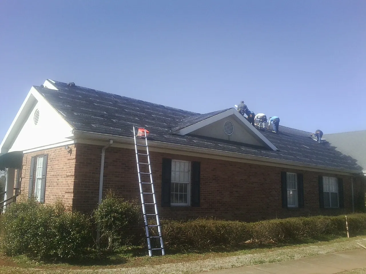 Crew tearing shingles off a brick ranch roof with a ladder set — Emergency Roof Repair work by our crew in Leawood