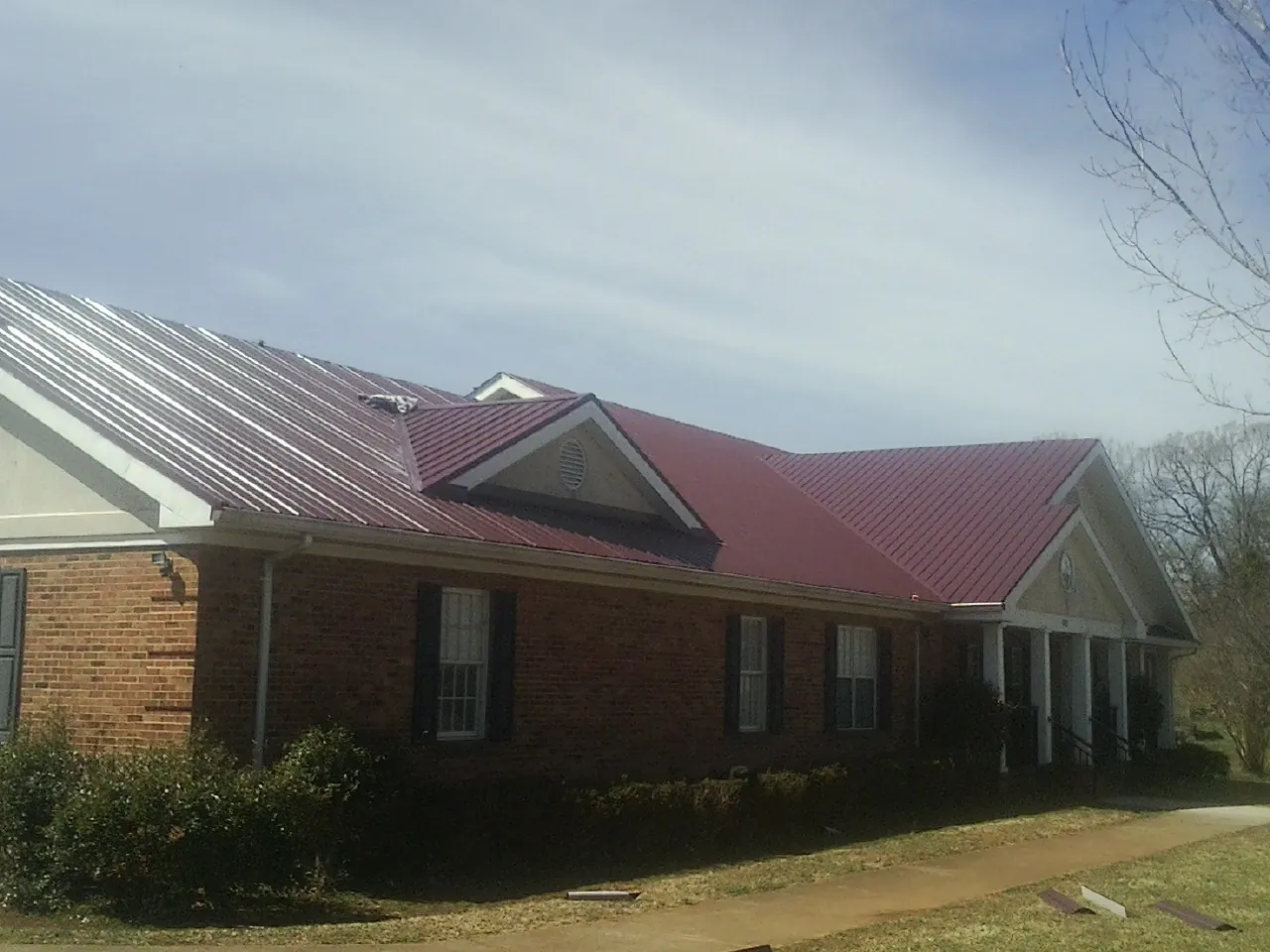 Red metal roof with gabled entries on a long brick building, from a Hail Damage Roof Repair job in Leawood