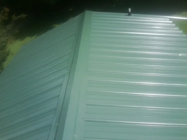 New green metal panels meeting at the ridge of a roof — Flat Roof Repair work by our crew in Leawood