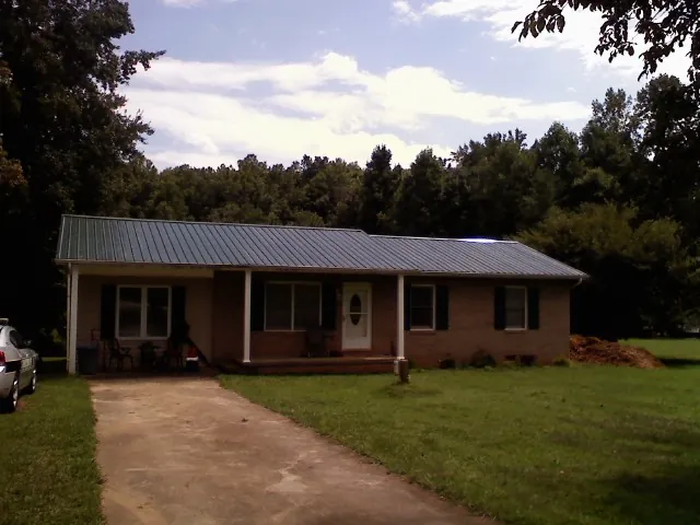 Dark green metal roof on a brick ranch with a covered porch in Leawood