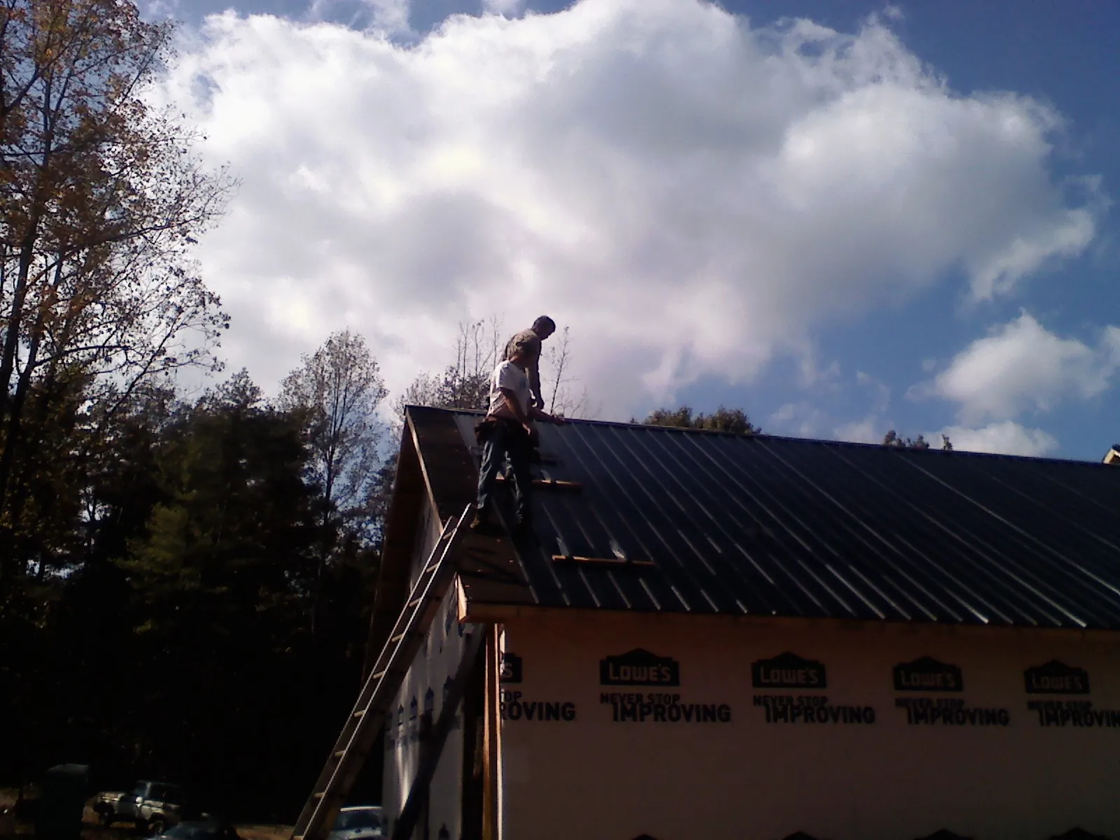 Roofer fastening dark metal panels high against a cloudy sky, from a Roof Inspection job in Leawood