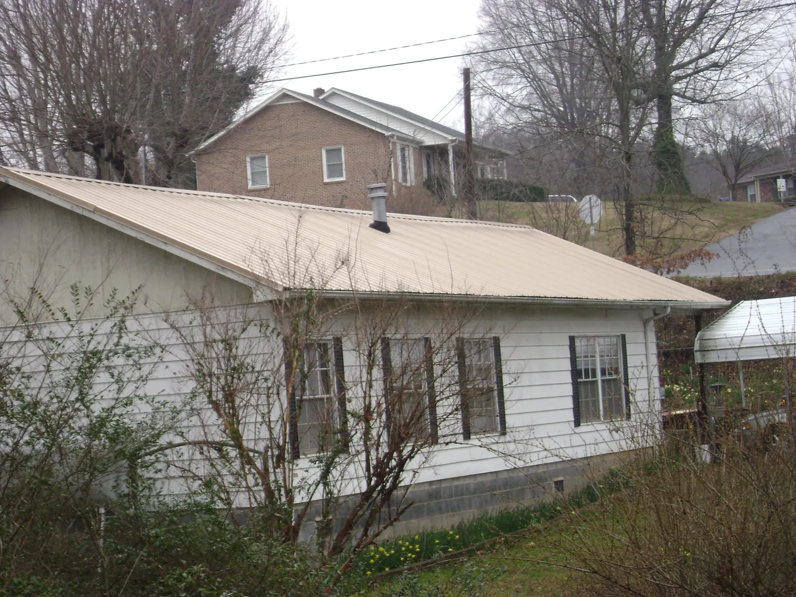 Tan metal roof on a white sided house set into a hillside — Commercial Roofing by Roofing Brothers in Leawood