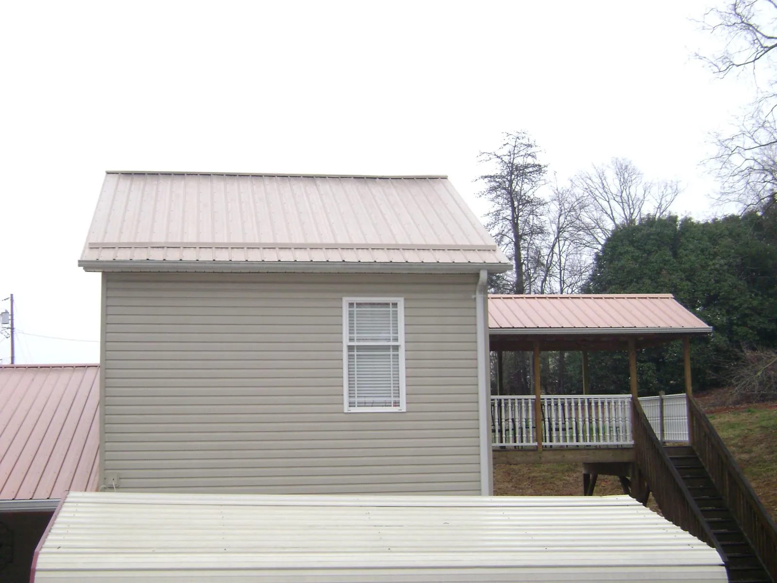 Tan metal roofs on a two story addition and attached porch, from a Roof Replacement job in Leawood